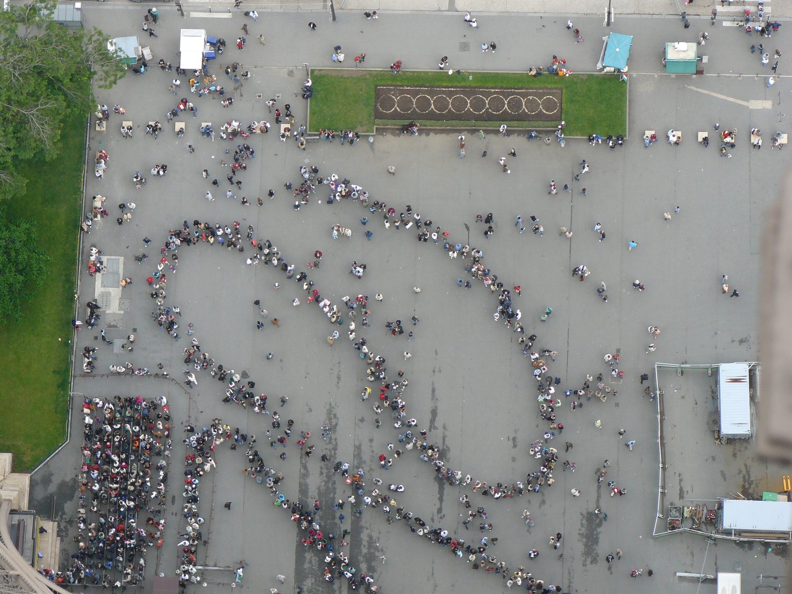 Vue aérienne d'une file d'attente qui serpente sur un parvis, au pied de la tour Eiffel.